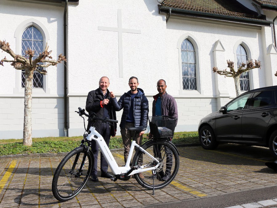 Übergabe des dritten E-Bikes durch den Projektleiter Nachhaltigkeit, Kevin Ischi, an Kirchenpflegepräsident Christian Palm und Sakristan Michael Yohannes in Zell. (v.l.n.r)