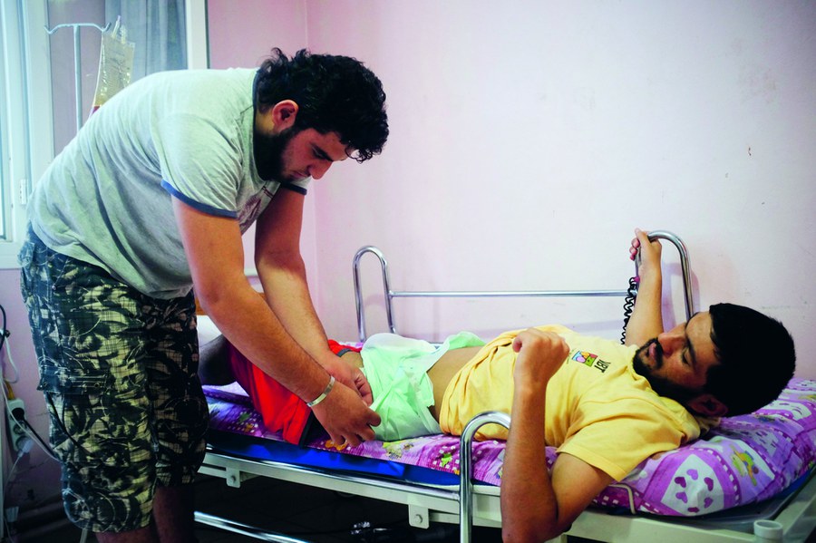 Spital Dar Alstshfaa, Türkei, Mai 2014: Die beiden Cousins Mohammed Azara (26) und Jeja Zougib (18) kämpften als Rebellen der FSA in Syrien. Im überlasteten Spital pflegt nun der ältere den verletzten jüngeren Kämpfer. Foto: Joseph Khakshouri