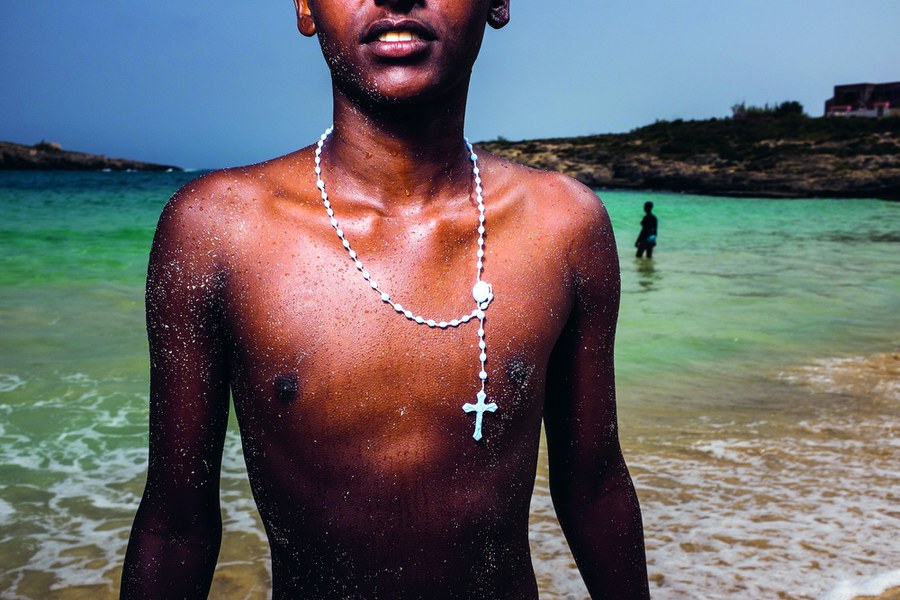 Lampedusa, Italien, April 2015: Junge Flüchtlinge spielen am Strand. Im Bild Meron Nagash (16), der mit dem Nachbarsjungen Abel Mikel (17) ohne Wissen ihrer Eltern aus Eritrea geflüchtet war: zunächst zu Fuss bis nach Äthiopien, dann drei Tage im Auto durch die Wüste Sudans. Schon nach dem ersten Tag ging ihnen das Wasser aus. Von Libyen auch überquerten sie dann in einem völlig überladenen Boot das Mittelmeer. Foto: Joseph Khakshouri